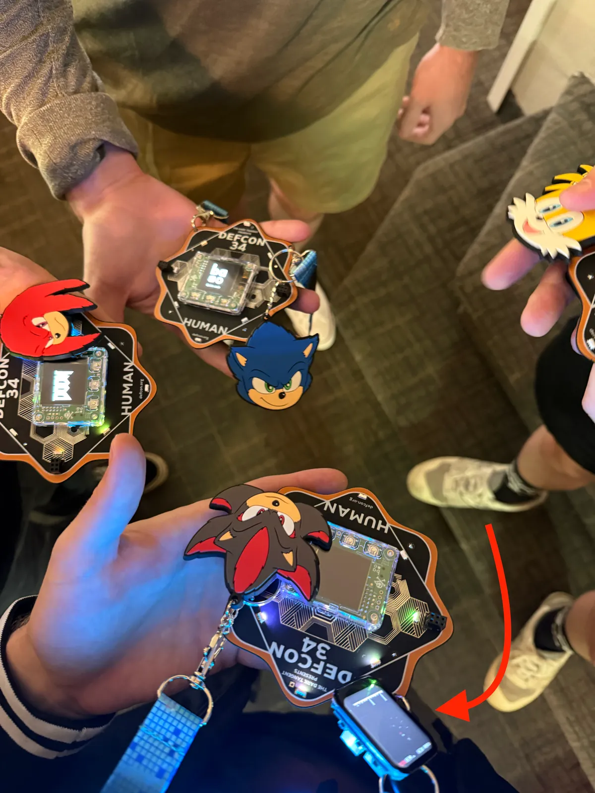 A cluster of DEF CON 34 badges held together, with an arrow pointing to the ESP32 device hanging below mine