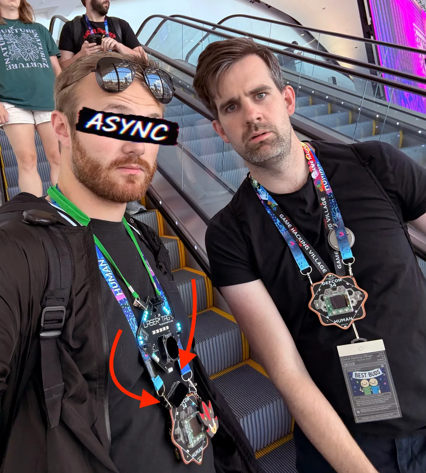 Wearing the Laser Tag badge on an escalator at DEF CON 34, with arrows pointing to the ESP32 device hanging from it
